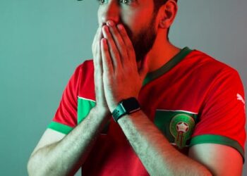 Le Football au Maroc : Histoire, Passion et Avenir des Lions de l'Atlas 3 A dynamic and vibrant image capturing the essence of Moroccan football, featuring the national team's 'Lions of the Atlas' emblem, a stadium filled with passionate fans holding Moroccan flags, and subtle architectural elements of Morocco in the background. The mood should be celebratory and full of national pride.